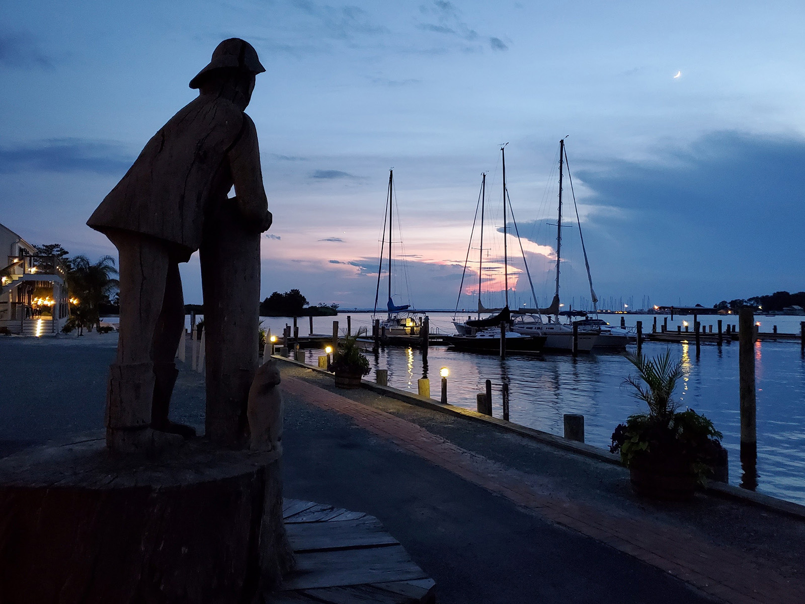 A statue of a fisherman overlooking a marina at twilight